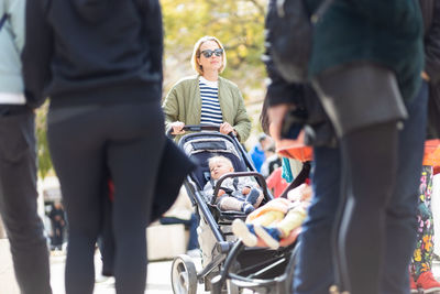 Mother walking and pushing his infant baby boy child in stroller in crowd of people wisiting sunday