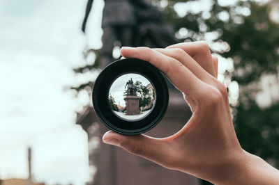 Close-up of hand holding camera against sky
