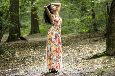 Young woman standing by tree in forest