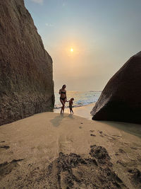 Rear view of woman walking on beach against sky during sunset