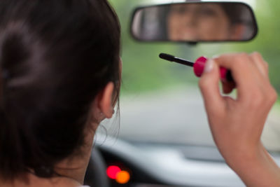 Reflection of woman applying make-up on rear-view mirror in car