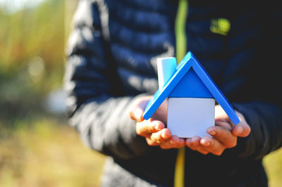 Midsection of man holding toy blocks forming model home