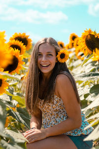 Portrait of smiling teenage girl sitting amidst sunflowers on land