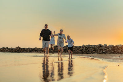 Rear view of man standing at beach against sky during sunset