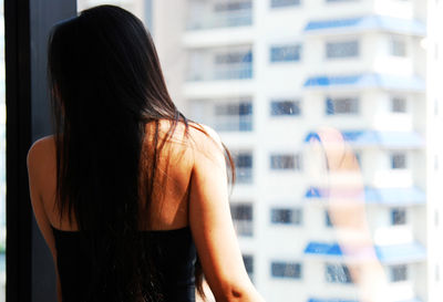 Rear view of woman standing by glass window