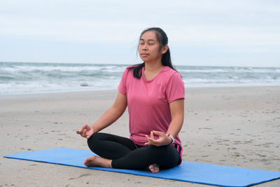 Portrait of young woman sitting at beach against sky