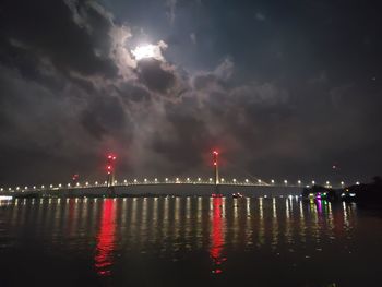 Illuminated bridge over river against sky at night