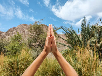 Midsection of woman praying hands against sky