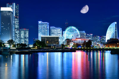 Illuminated city by river against sky at night