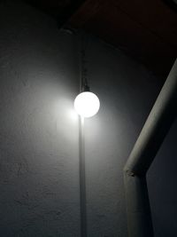 Low angle view of illuminated light bulb against wall
