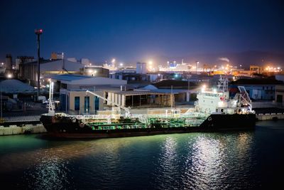 Boats moored in illuminated harbor against sky at night