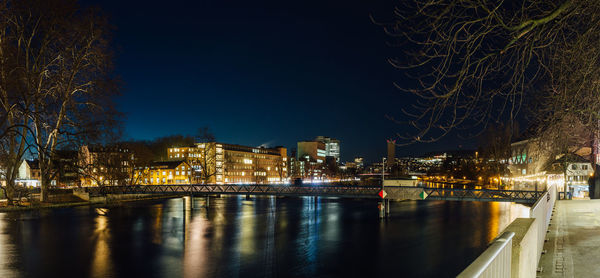 Illuminated city by river against sky at night
