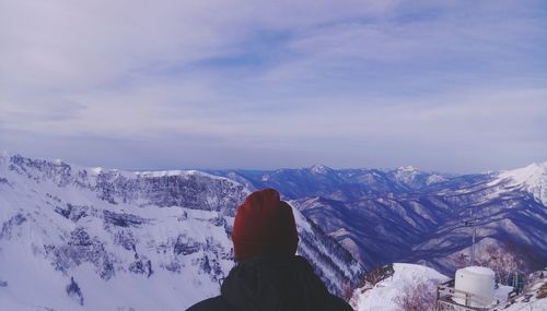 Rear view of person in warm clothing against snowcapped mountain