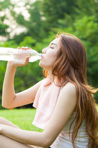 Woman drinking water from bottle against trees