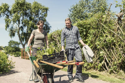 Happy couple walking with loaded wheelbarrow at community garden