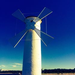 Low angle view of windmill on landscape against blue sky