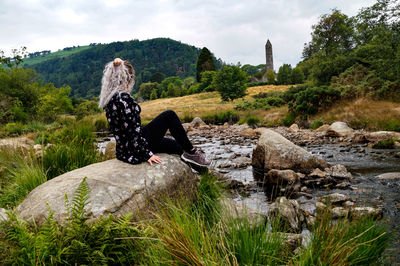 Man sitting on rock by lake against sky