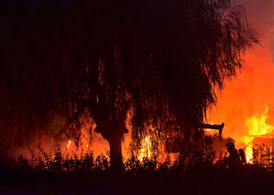 Anonymous fireman in uniform putting out bright fire in woods at dark night