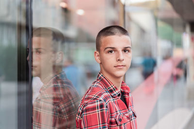 Portrait of young man standing against window