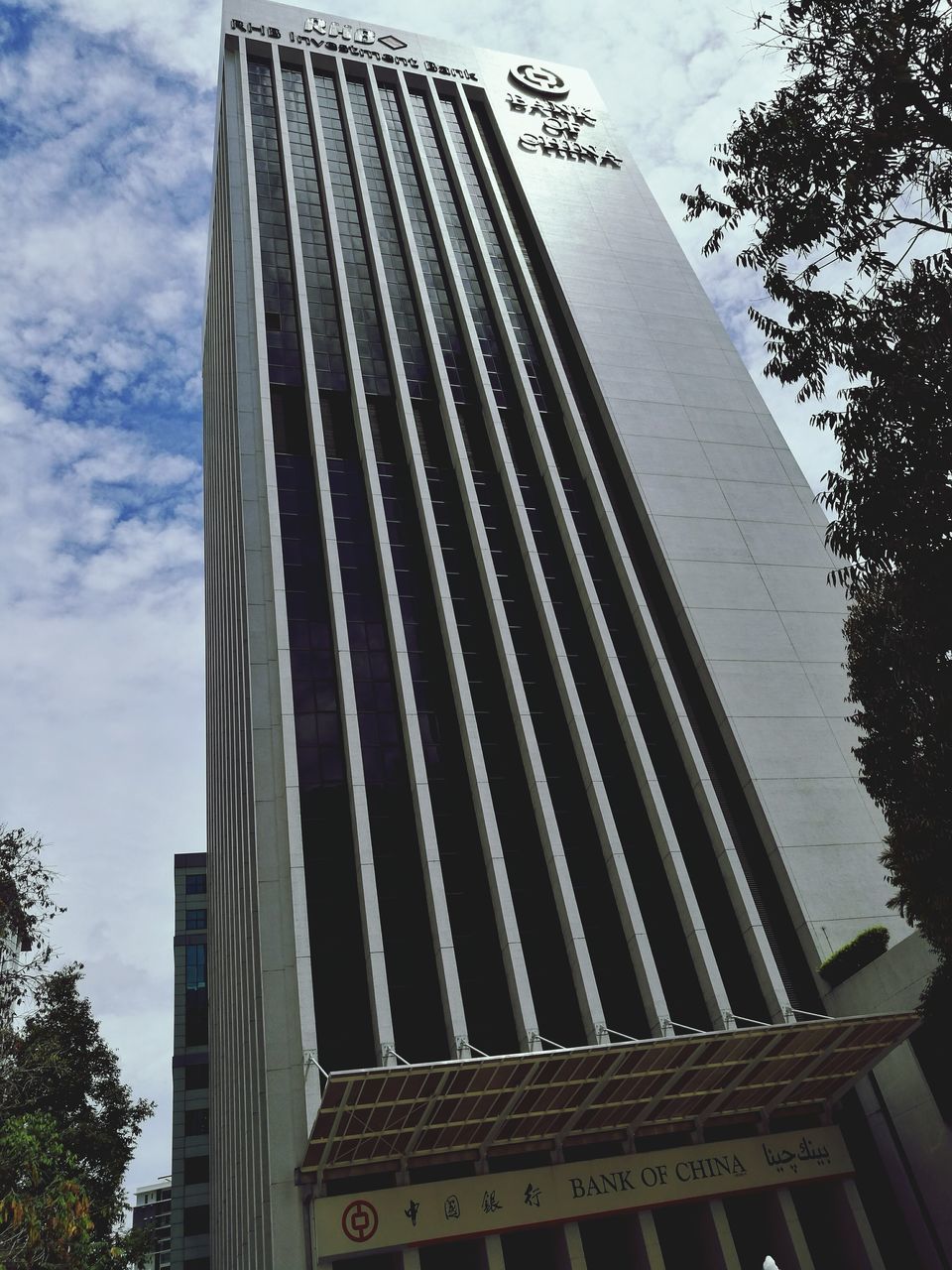 architecture, building exterior, built structure, low angle view, tree, modern, city, office building, tall - high, skyscraper, sky, reflection, tall, tower, cloud, outdoors, day, city life, place of work, building story, no people, office block, development, high section, architectural feature, cloud - sky