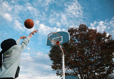 Woman throwing ball in basketball hoop against sky
