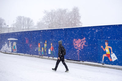 Full length of man walking on snow covered field against sky