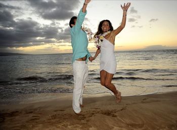 Full length of young woman enjoying at beach against sky during sunset