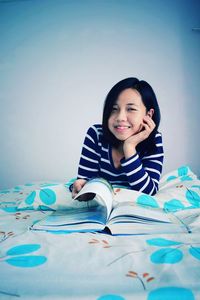Portrait of young woman reading book while sitting on bed at home