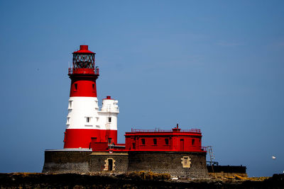 Lighthouse by sea against clear sky