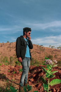 Full length of young man standing on land against cloudy sky