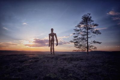 Wooden mannequin standing on landscape during sunset