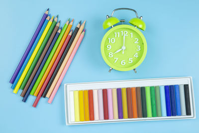 Multi colored art and craft equipment with alarm clock over blue background