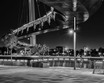 Illuminated bridge by buildings against sky at night