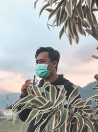 Portrait of young man holding drink against sky