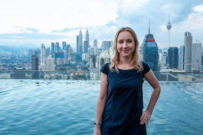 Portrait of young woman standing against buildings in city