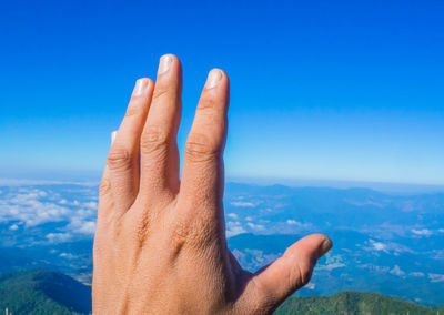 Cropped hand against blue sky