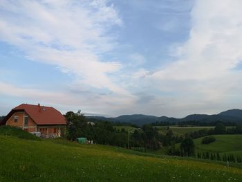 House on field by houses against sky
