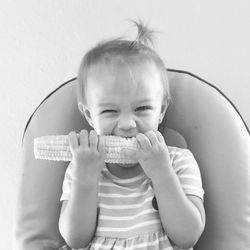 Portrait of smiling girl eating corn on seat at home