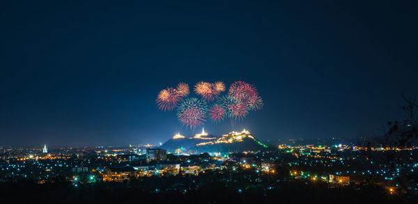 Firework display in city against sky at night