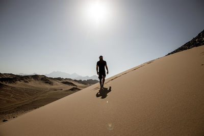 A man walks in the direction of the camera on a sand dune