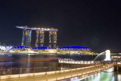 Illuminated bridge over river against buildings at night