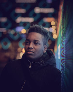 Thoughtful young man looking away against defocused lights