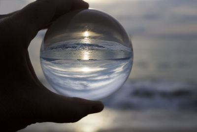 Cropped hand holding crystal ball against sea