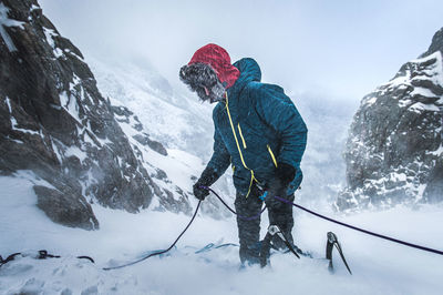 Male alpine climber belays his lead climber as snow blows in the cold