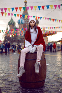 Woman in a sweater sits in winter on a large barrel in moscow on red square on christmas day
