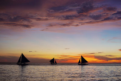 Silhouette sailboats in sea against sky during sunset