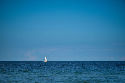 Sailboat sailing in sea against blue sky