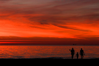 Silhouette people looking at sea against orange sky