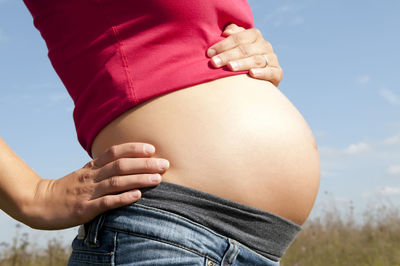 Midsection of woman with arms raised against sky