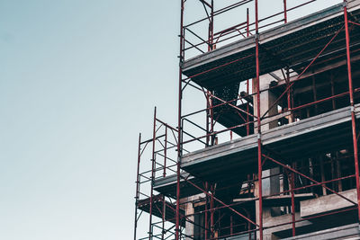 Low angle view of crane against building against clear sky